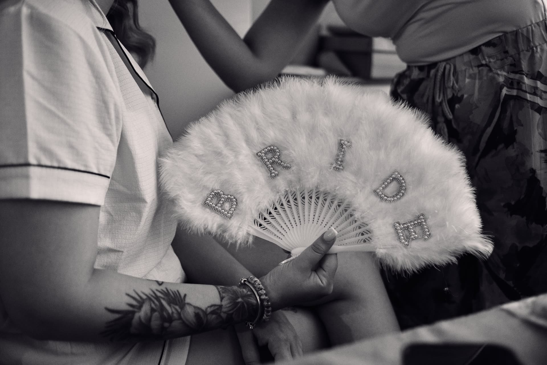 A bride preparing with a fan in soft monochrome light