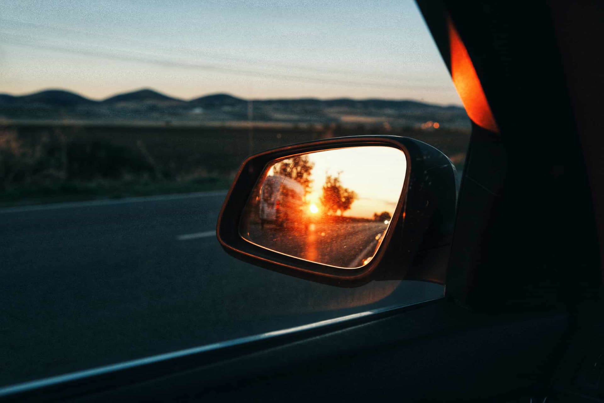 Sunset reflected in a car mirror on an open road